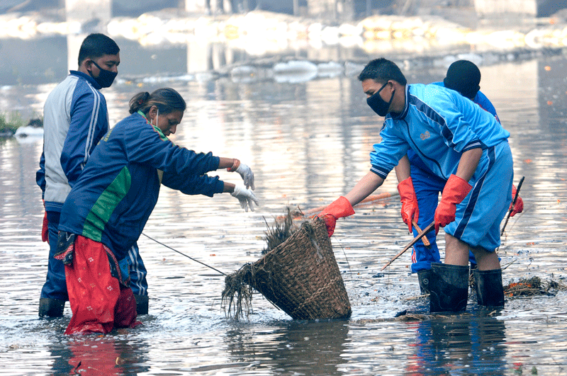 Volunteers wading into a polluted waterway to clear plastic waste and weeds by hand